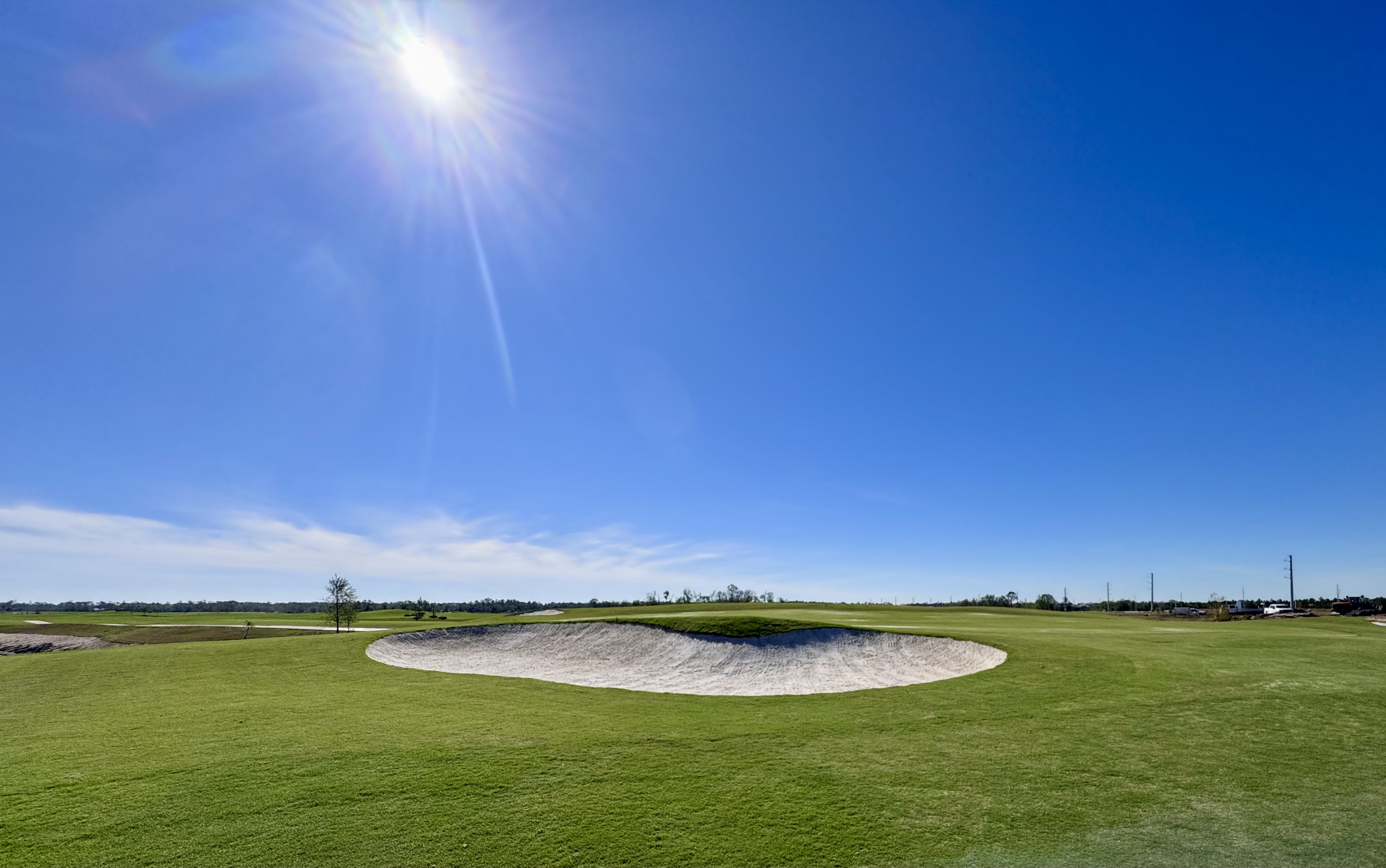 The sun shines brightly above a sand pit surrounded by vibrant greens.