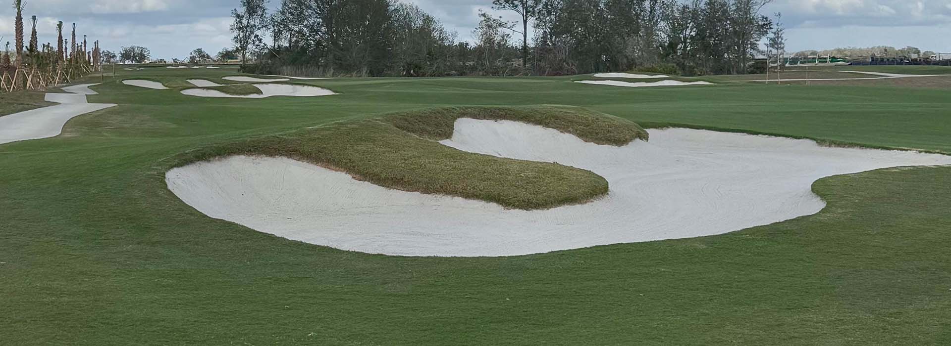 A white sand pit in the center, cloudy skies, and well maintained grass covers the land.